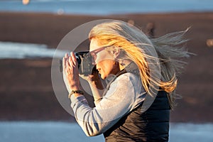 A woman with a DSLR takes an outdoor picture on a windy sunset evening.