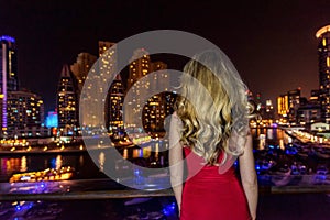 Woman in Dubai Marina, United Arab Emirates. Attractive lady wearing a red dress. Girl admiring Marina view at nights