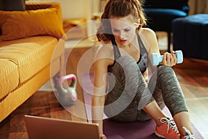 Woman with dumbbell using laptop to share workout results