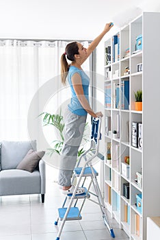 Woman dusting a bookcase at home
