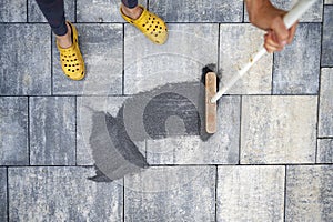 Woman dusting special sand for tile gap into the spaces between outside tiles