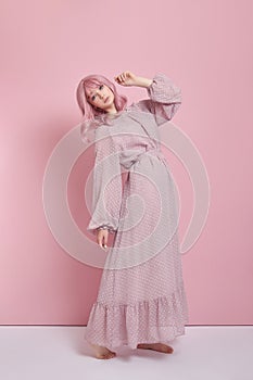 Woman with dyed pink hair in a long dress. Portrait of a girl with hair coloring at the pink wall. Perfect hairstyle and hair