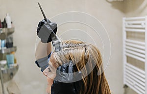 A woman dyes her hair in her home bathroom.