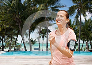 woman with earphones and armband jogging on beach