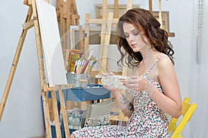 Woman with easel, palette and brush painting at art studio