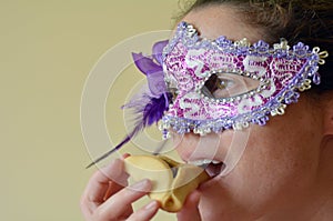 Woman eat Hamantaschen cookie and wearing Purim Mask