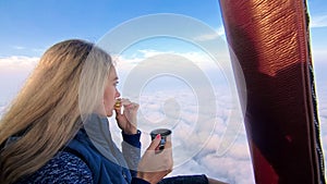 Woman eat sandwich and drinks tea and coffee in flight. Adventure on hot air balloon. Fly in morning blue sky above