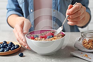 Woman eating acai smoothie with granola and berries at grey table