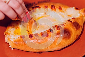 Woman is eating adjarian khachapuri with hands, crushing egg yolk.