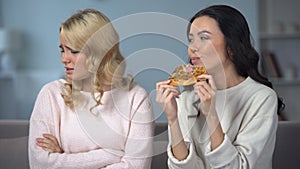 Woman eating appetizing pizza while friend fighting with fast food eating desire