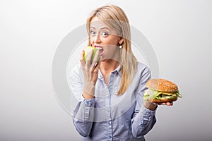 Woman eating apple and holding a burger