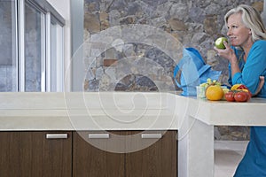 Woman Eating Apple At Kitchen Counter