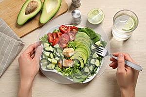 Woman eating avocado salad with fried chicken at wooden table, top view