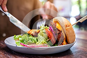 Woman eating beef hamburger with knife and fork