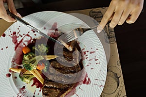 Woman eating beef steak `Striploin` in wine sauce, isolated on a table. Healthy lunch at the restaurant on the wooden table. Fem