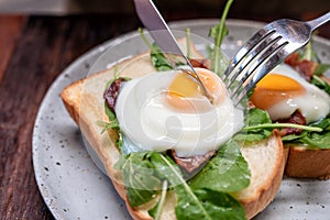 A woman eating breakfast sandwich with eggs, bacon and sour cream by knife and fork in a plate