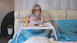 Woman Eating Breakfast Sausages With Fried Eggs On The Table, Lying In Bed