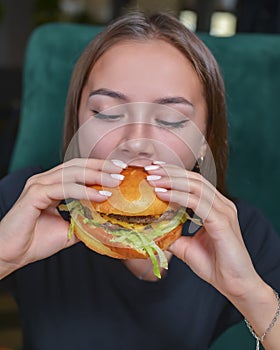 Woman eating burger and fries smiling. Beautiful caucasian female model eating a hamburger with hands