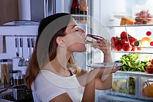 Woman Eating Cake In Front Of Refrigerator