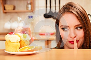 Woman eating cake showing quiet sign. Gluttony.