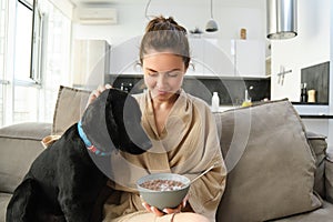 Woman eating cereals with dog on sofa