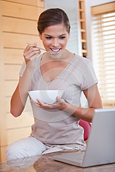 Woman eating cereals next to her laptop