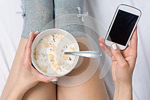 Woman eating cereals and texting in bed