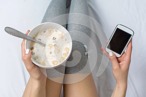 Woman eating cereals and texting in bed