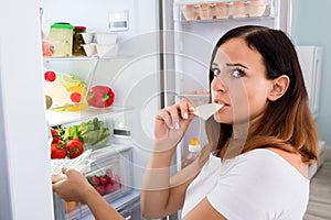 Woman Eating Cheese In Front Of Refrigerator