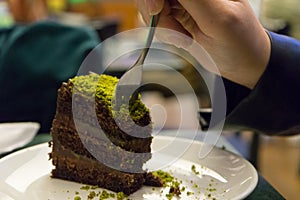 Woman eating chocolate cake with pistachio, taking a piece on a slice of cooked dessert in a restaurant. Hand with Fork taste