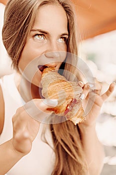 A woman is eating a croissant. The croissant is half eaten and has a jelly filling.