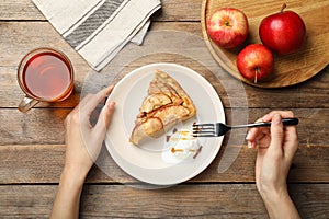 Woman eating delicious apple pie with ice cream at wooden table, top view