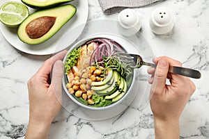 Woman eating delicious avocado salad with chickpea at marble table, top view