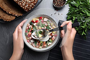 Woman eating delicious cold okroshka with kvass at grey table. Traditional Russian summer soup