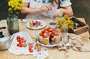 Woman eating a delicious home-made cake with aisheny and stuffed strawberries for dessert. Summer Styled dinner table. Coffee to