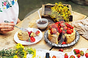 Woman eating a delicious home-made cake with aisheny and stuffed strawberries for dessert. Summer Styled dinner table. Coffee to