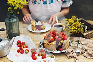 Woman eating a delicious home-made cake with aisheny and stuffed strawberries for dessert. Summer Styled dinner table. Coffee to