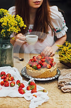 Woman eating a delicious home-made cake with aisheny and stuffed strawberries for dessert. Summer Styled dinner table. Coffee to