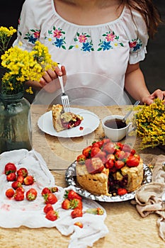Woman eating a delicious home-made cake with aisheny and stuffed strawberries for dessert. Summer Styled dinner table. Coffee to