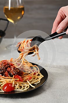 Woman eating delicious pasta with meatballs and tomato sauce at table, closeup