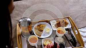 Woman is eating desserts in bed from wooden tray in hotel room on vacations.