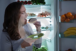 Woman Eating Donut In Front Of Fridge
