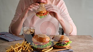 Woman eating Fast food. Burgers, french fries, cola. A woman made a hamburger from buns, cutlets, lettuce, cucumber