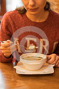 Woman eating fish soup with salmon, sea bass and herbs at seafood cafe. Female hand holds a full spoon over a soup bowl.