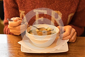 Woman eating fish soup with salmon, sea bass and herbs at seafood cafe. Female hand holds a full spoon over a soup bowl.