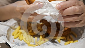Woman eating french fries, chicken and burger in fast food cafe, food closeup.