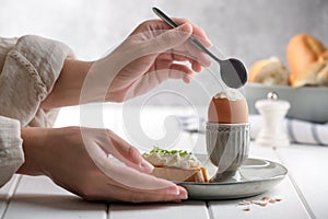 Woman eating fresh soft boiled egg at white wooden table, closeup