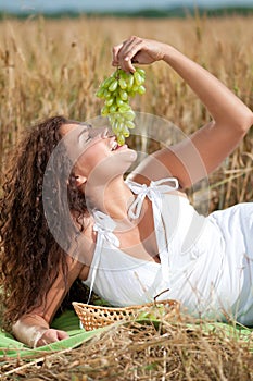 Woman eating grapes in wheat field. Picnic.