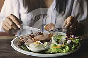 A woman eating grilled sausage, in morning