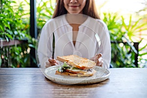 A woman eating ham cheese sandwich by knife and fork